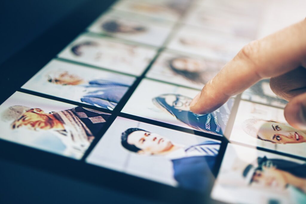 Human resources and marketing concept. Head shots displayed on a tablet with a hand making a selection.